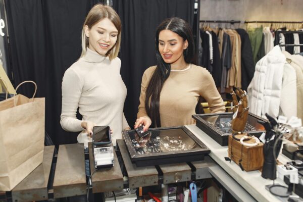 Two women making a contactless payment with smiles at a jewelry store counter.